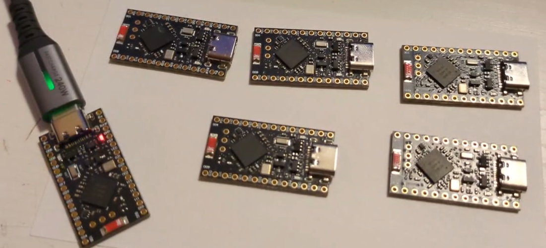 Six NRF chips lined up on my desk, ready to be flashed, with one plugged into a USB-C cable off to the side